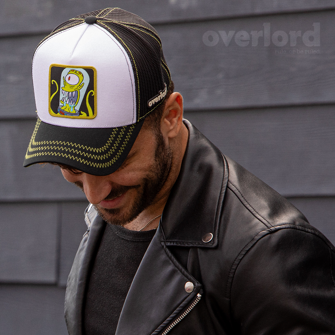 Man wearing white and black OVERLORD X The Simpsons present Kang the alien trucker baseball cap hat with lime green zig zag stitching. PVC Overlord logo.