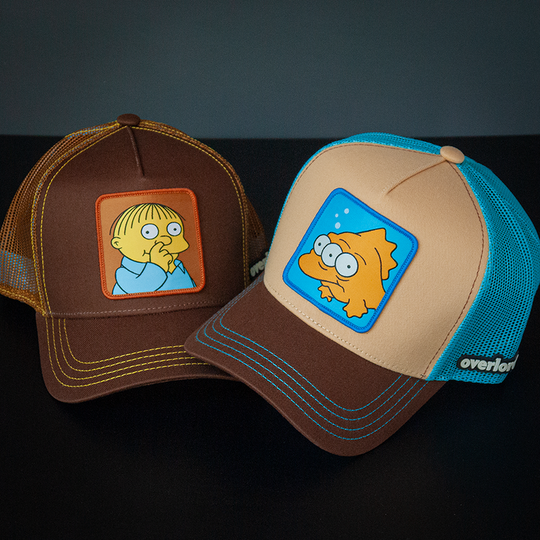 Tan and brown OVERLORD X The Simpsons Blinky the three-eyed fish trucker cap hat with aqua zig zag stitching. PVC Overlord logo.