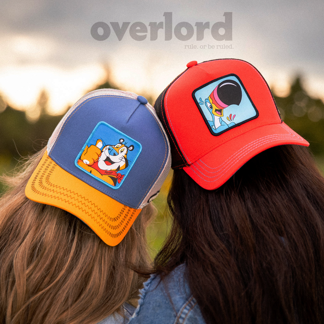 Woman wearing red OVERLORD X Kelloggs Toucan Sam Froot Loops trucker baseball cap hat with blue stitching. PVC Overlord logo.