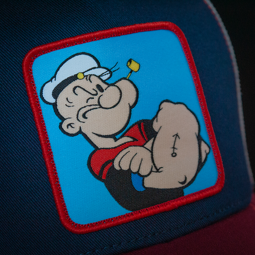 Navy and red OVERLORD X Popeye smug Popeye trucker baseball cap hat woven Overlord patch closeup.