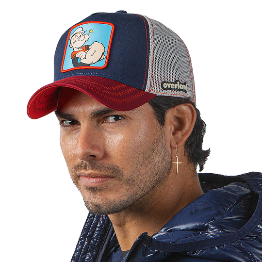 Man wearing navy and red OVERLORD X Popeye smug Popeye trucker baseball cap hat with red zig zag stitching. PVC Overlord logo.