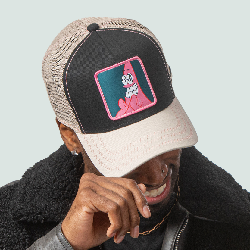 Man wearing black and tan OVERLORD X SpongeBob Big Smile Patrick trucker baseball cap hat with pink zig zag stitching. PVC Overlord logo.