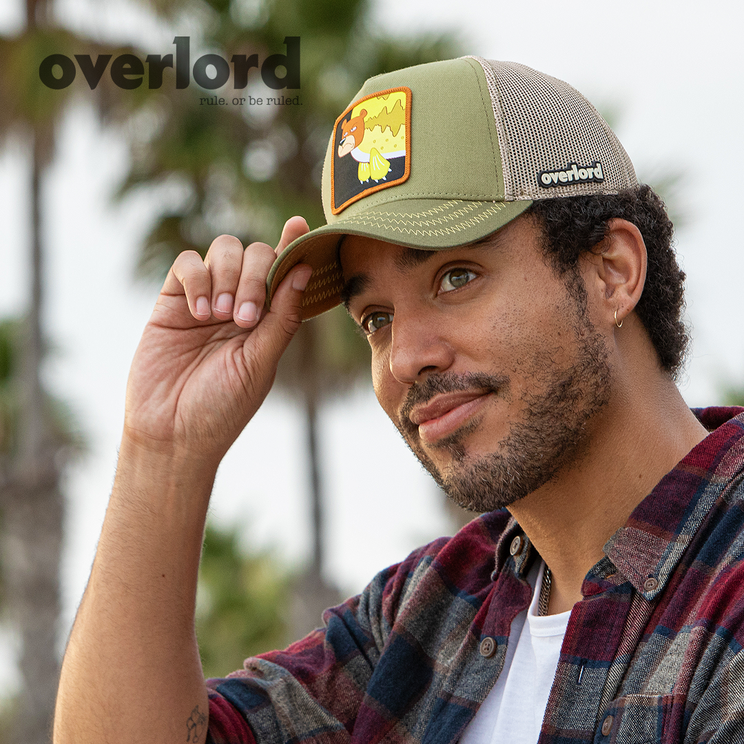 Man wearing olive green OVERLORD X SpongeBob Seabear trucker baseball cap hat with light olive zig zag stitching. PVC Overlord logo.