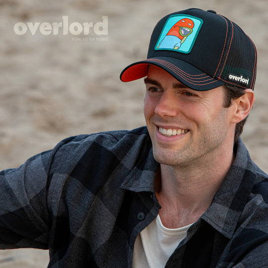 Man wearing black OVERLORD X SpongeBob Load of Barnacles fish trucker baseball cap hat with red orange stitching. PVC Overlord logo.