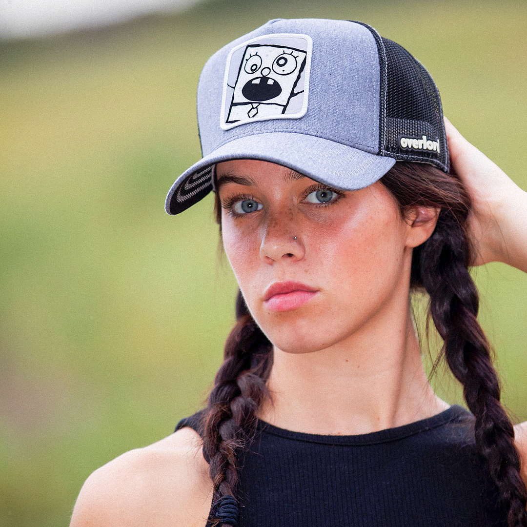 Woman wearing heather gray OVERLORD X SpongeBob DoodleBob trucker baseball cap hat with light gray zig zag stitching. PVC Overlord logo.