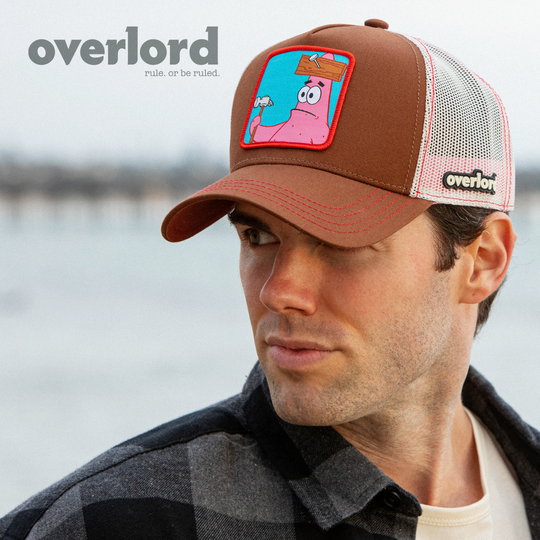 Man wearing brown OVERLORD X SpongeBob Patrick holding hammer trucker baseball cap hat with red stitching. PVC Overlord logo.