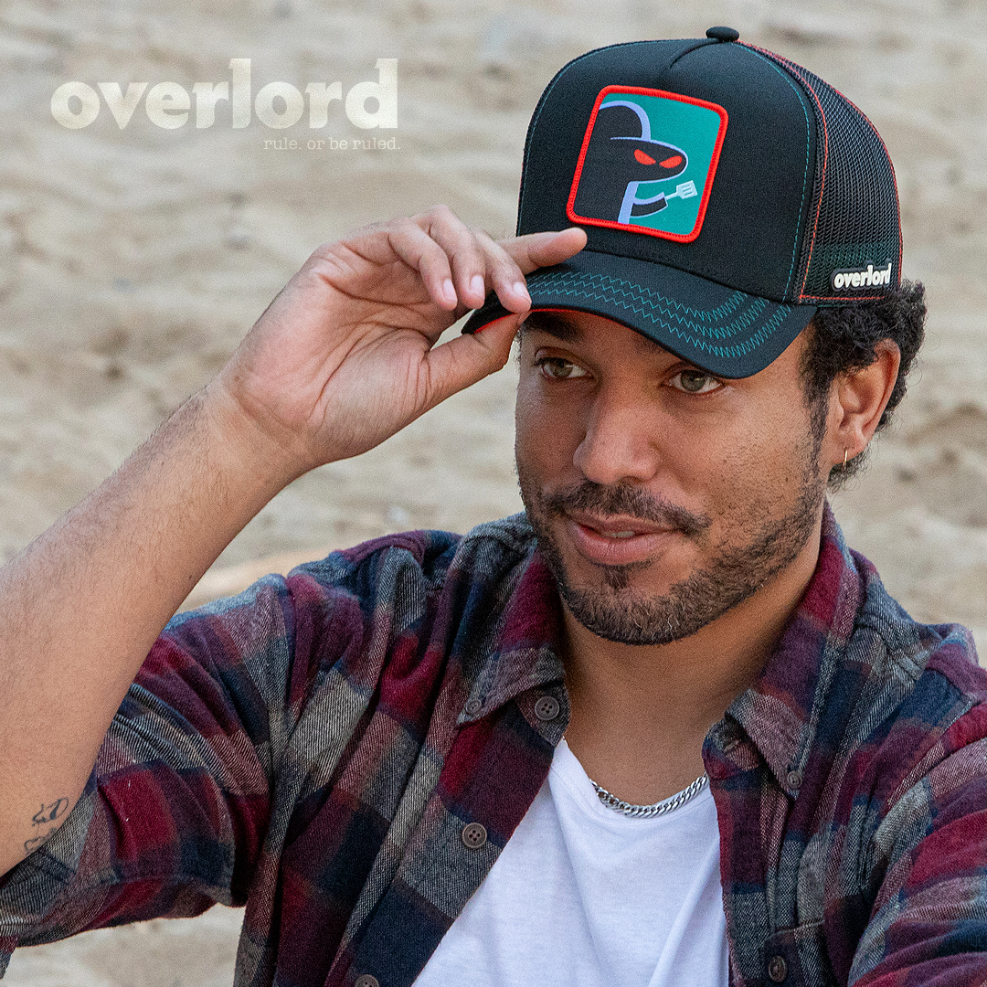 Man wearing black OVERLORD X SpongeBob Hash Slinging Slasher trucker baseball cap hat with teal zig zag stitching. PVC Overlord logo.