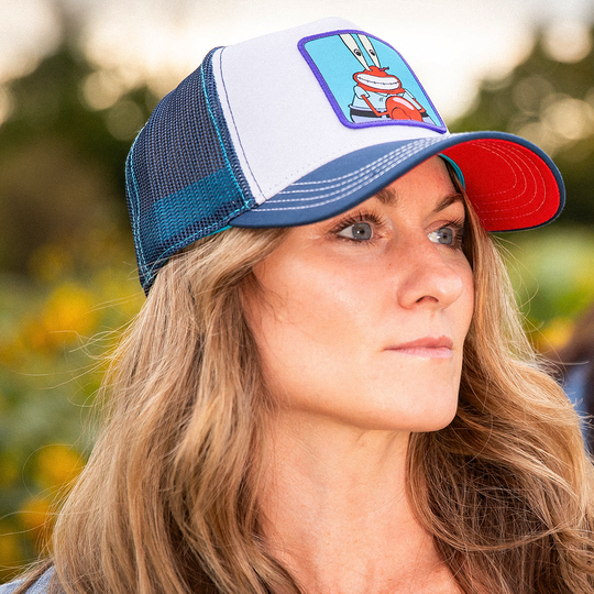 Woman wearing white and navy OVERLORD X SpongeBob Krusty Krab trucker baseball cap hat with cream stitching. PVC Overlord logo.