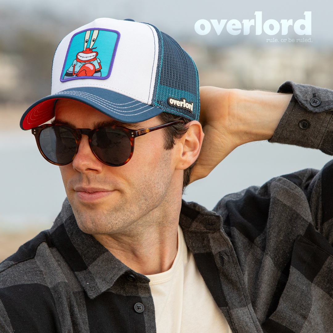 Man wearing white and navy OVERLORD X SpongeBob Krusty Krab trucker baseball cap hat with cream stitching. PVC Overlord logo.