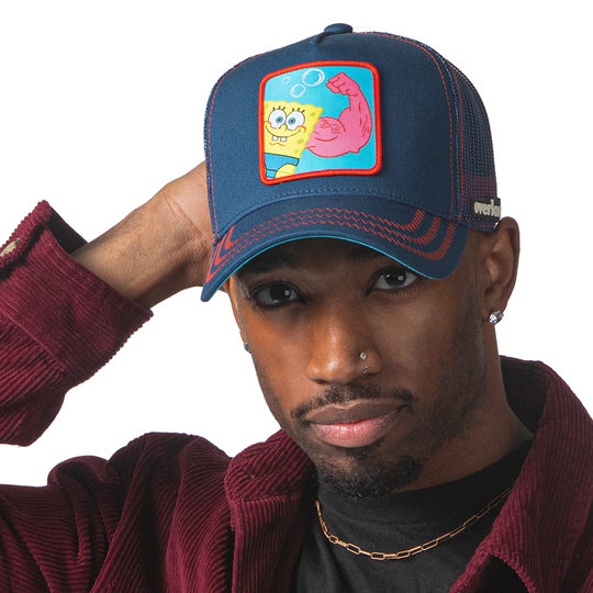Man wearing navy OVERLORD X SpongeBob MuscleBob trucker baseball cap hat with red zig zag stitching. PVC Overlord logo.
