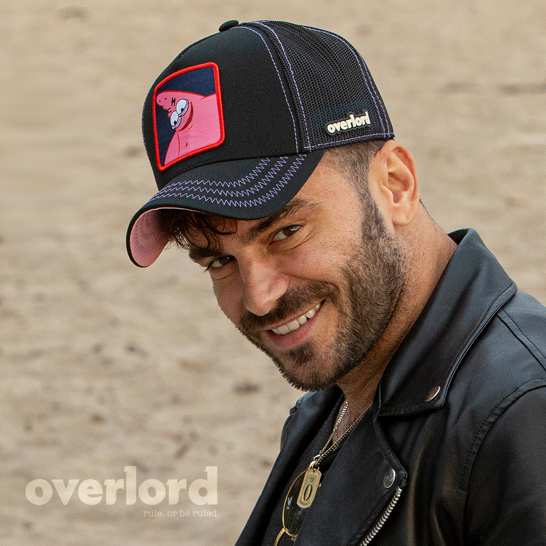 Man wearing black OVERLORD X SpongeBob Savage Patrick trucker baseball cap hat with purple zig zag stitching. PVC Overlord logo.