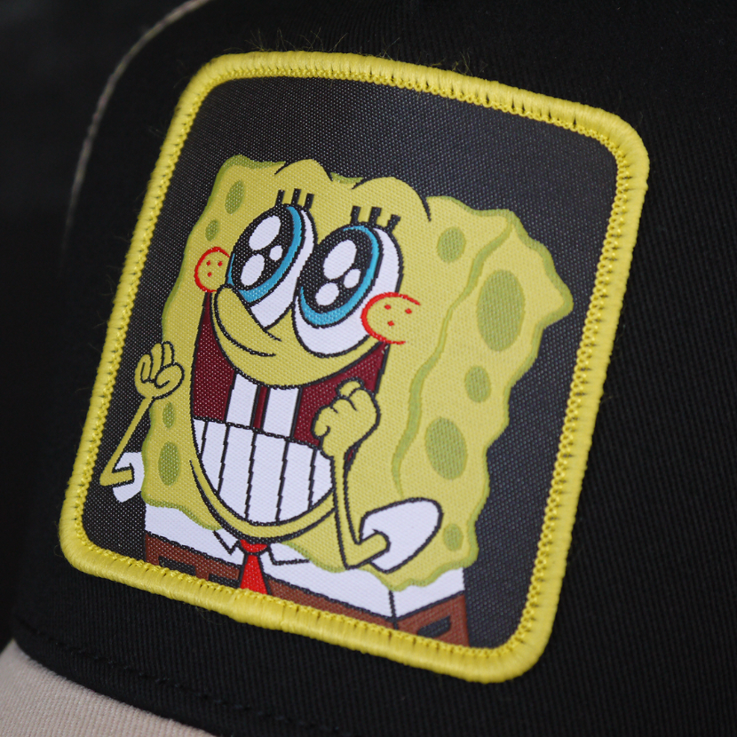 Black and tan OVERLORD X SpongeBob Big Smile SpongeBob trucker baseball cap hat woven Overlord patch closeup.