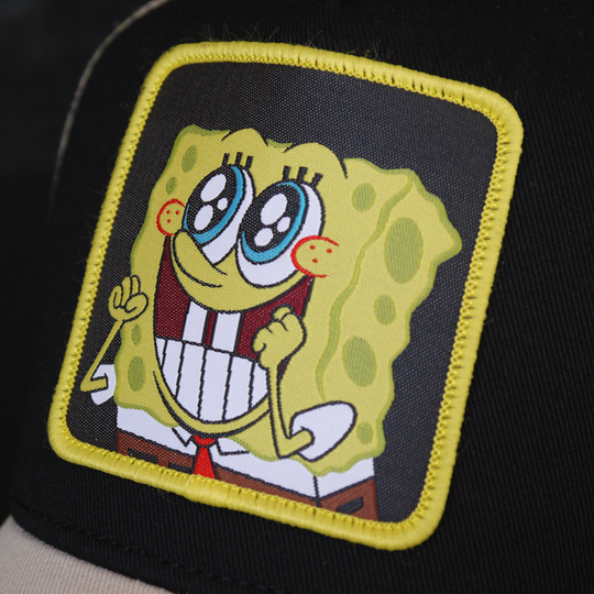 Black and tan OVERLORD X SpongeBob Big Smile SpongeBob trucker baseball cap hat woven Overlord patch closeup.