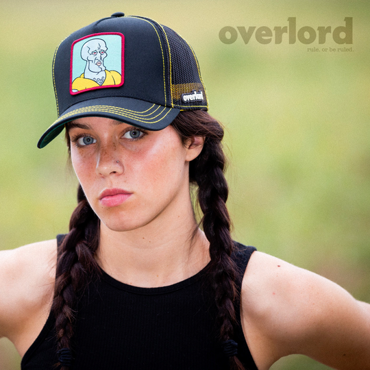Woman wearing black OVERLORD X SpongeBob Handsome Squidward trucker baseball cap hat with yellow stitching. PVC Overlord logo.