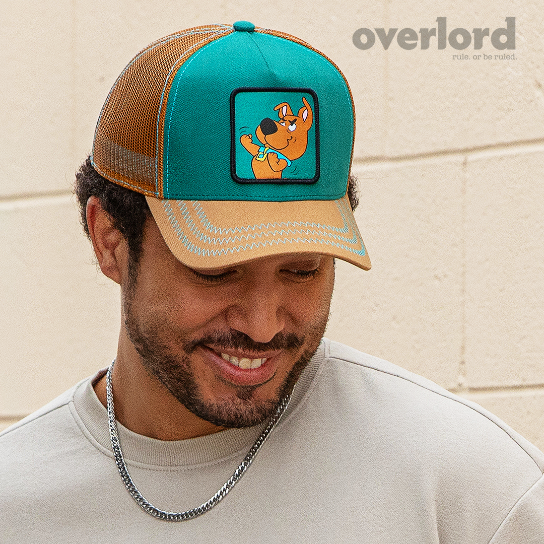 Man wearing teal and light brown Scooby-Doo fighting Scrappy trucker baseball cap hat with turquoise zig zag stitching. PVC Overlord logo.