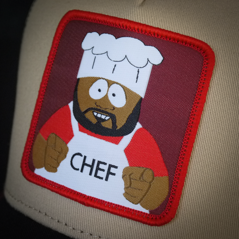 Tan and black OVERLORD X South Park Chef trucker baseball cap hat woven Overlord patch closeup.