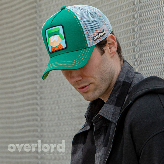 Man wearing green OVERLORD X South Park Kyle trucker baseball cap hat with orange stitching. PVC Overlord logo.