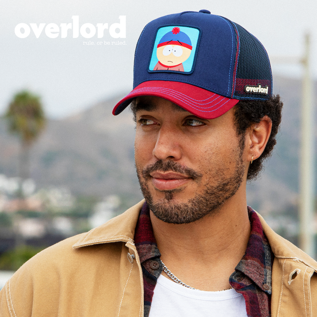 Man wearing navy and red OVERLORD X South Park Stan trucker baseball cap hat with blue stitching. PVC Overlord logo.