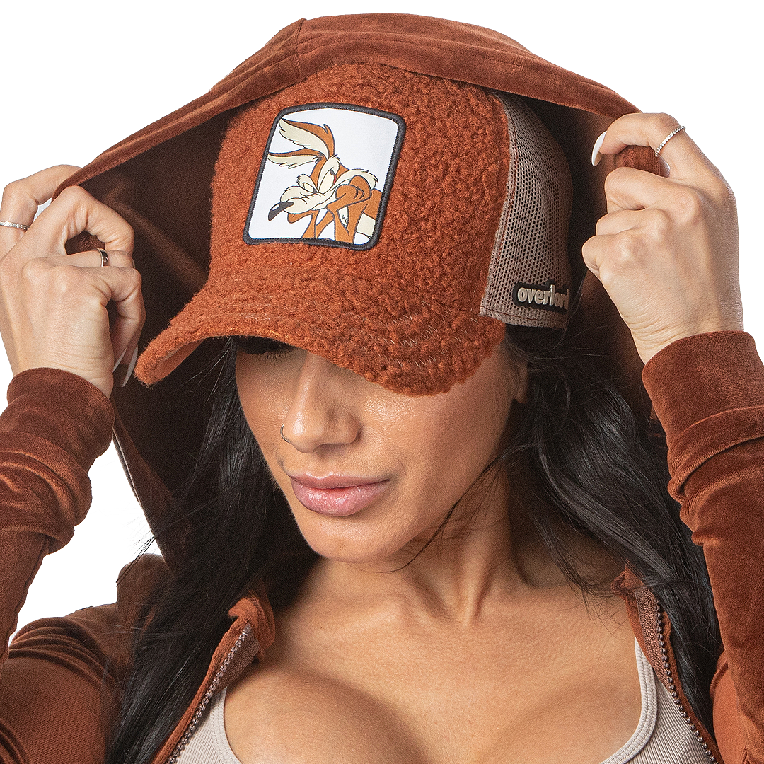 Woman in brown hoodie wearing brown sherpa OVERLORD X Looney Tunes Wile E. Coyote trucker baseball cap hat.